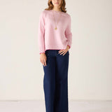 Woman wearing a pink sweater and navy pants against a white background
