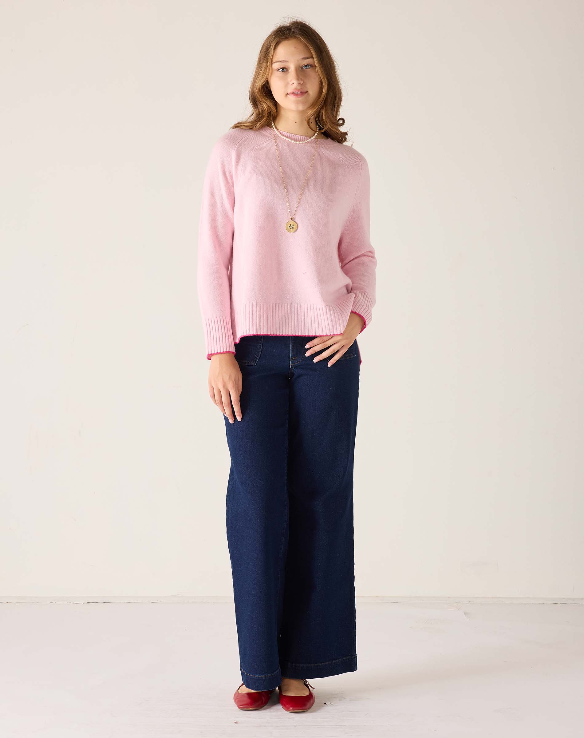 Woman wearing a pink sweater and navy pants against a white background