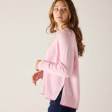 Woman wearing a pink sweater and blue jeans against a plain background