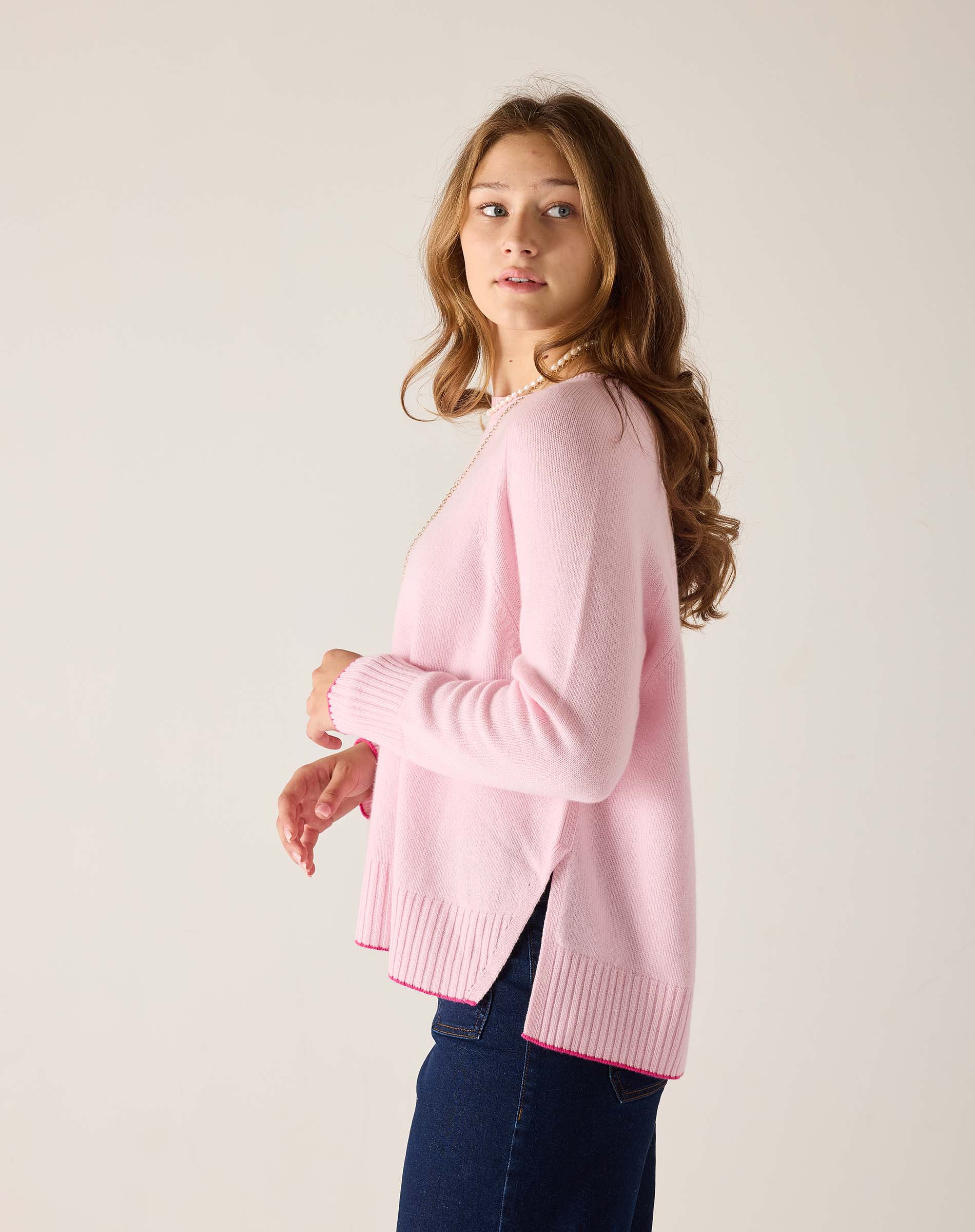 Woman wearing a pink sweater and blue jeans against a plain background