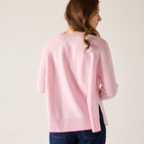 Woman wearing a pink sweater and blue jeans against a plain background