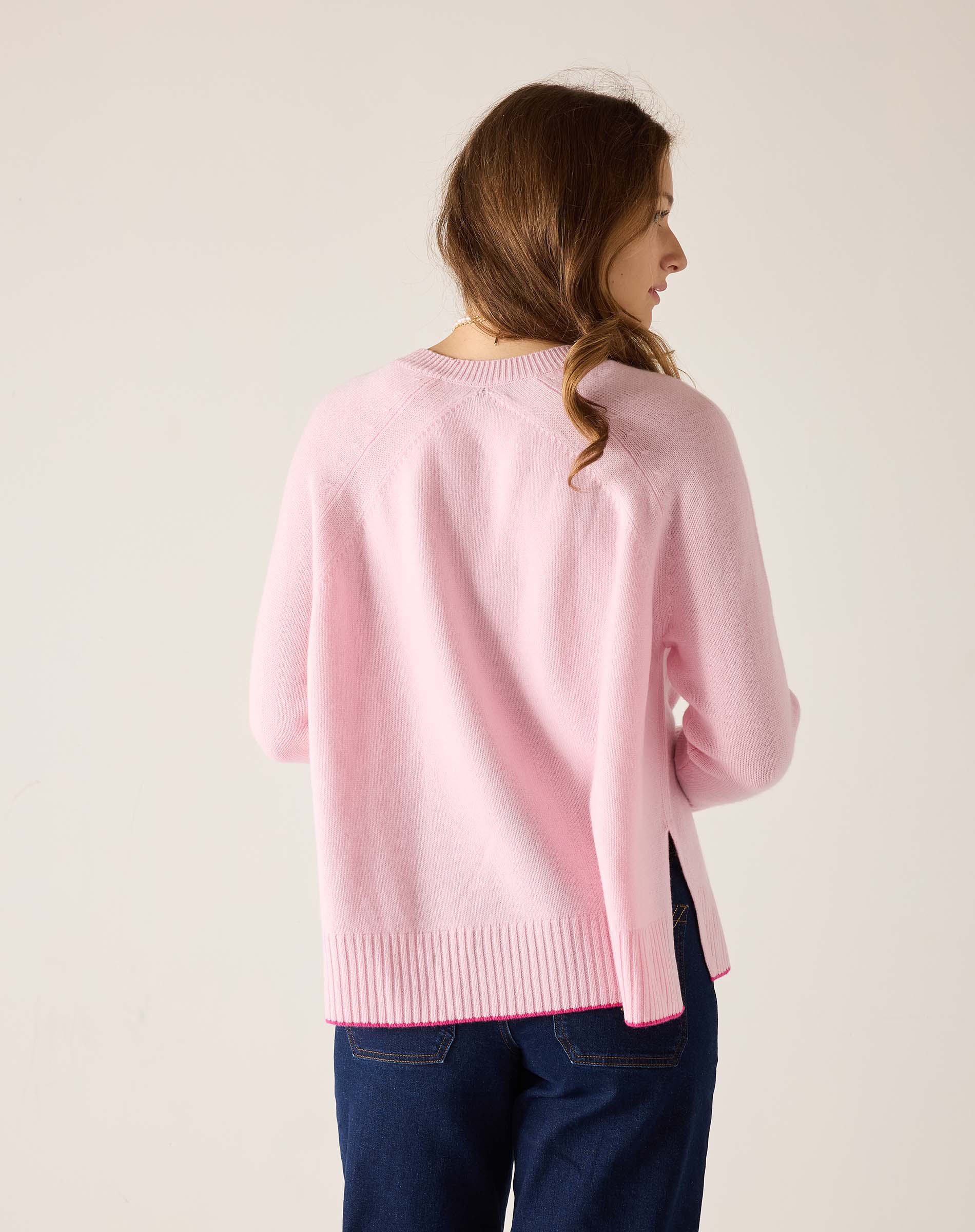 Woman wearing a pink sweater and blue jeans against a plain background