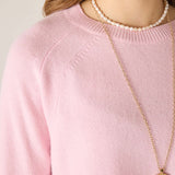 Person wearing a pink sweater with a pearl necklace and gold pendant.