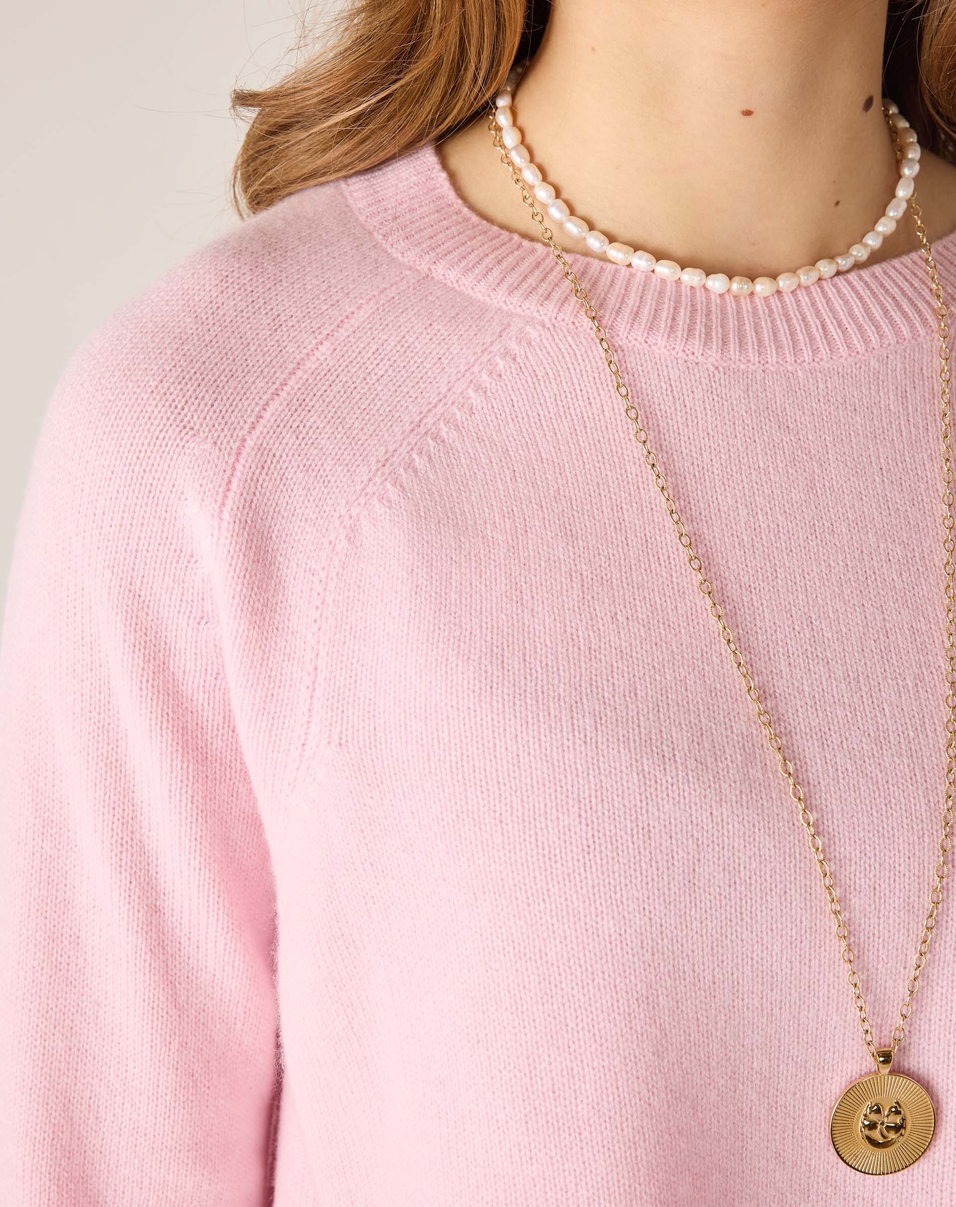 Person wearing a pink sweater with a pearl necklace and gold pendant.