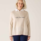 Woman wearing a beige sweater with text, standing against a plain background