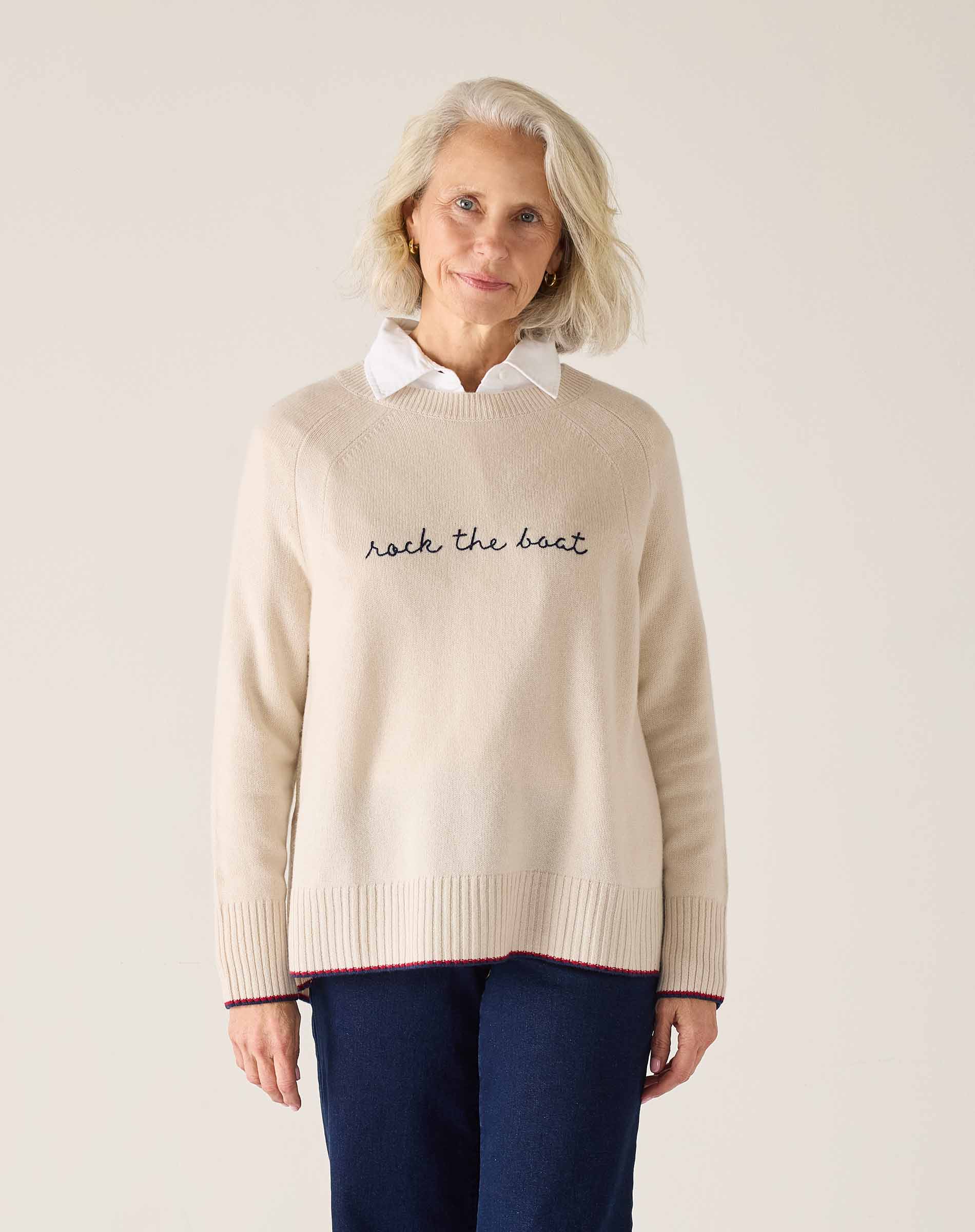 Woman wearing a beige sweater with text, standing against a plain background
