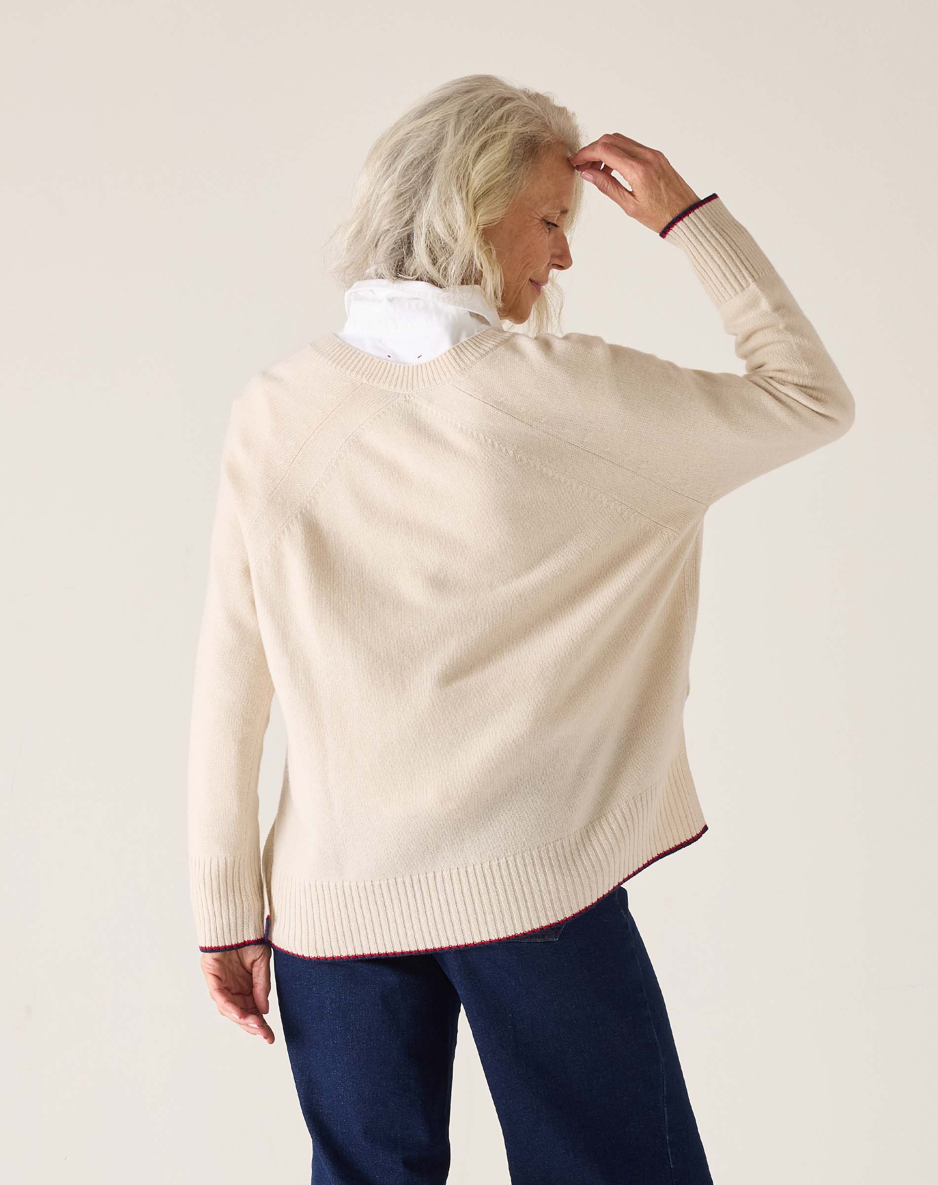 Person wearing a beige sweater with a white collar against a plain background