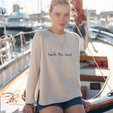 Woman wearing a white sweater with 'rock the boat' text on a boat.