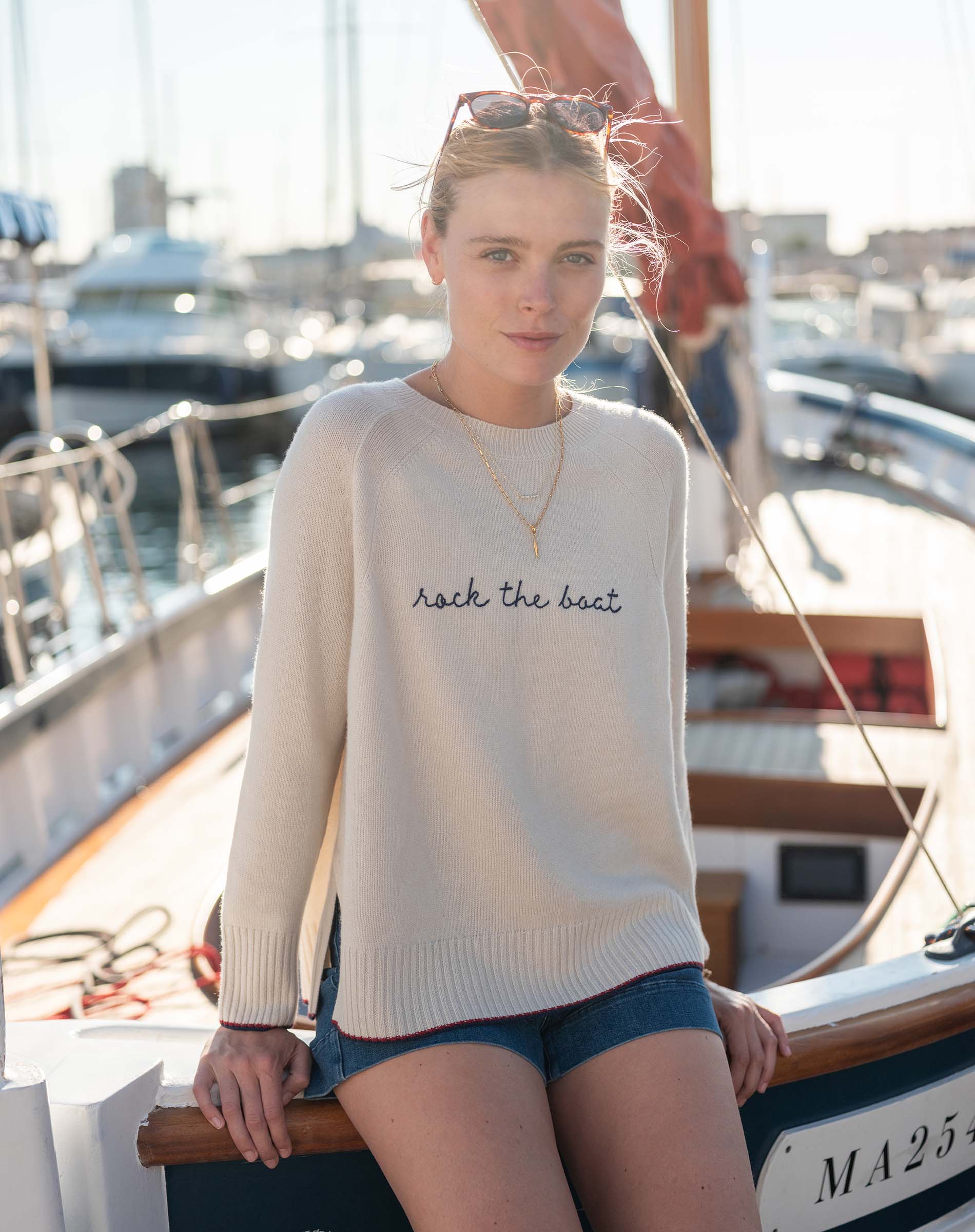 Woman wearing a white sweater with 'rock the boat' text on a boat.