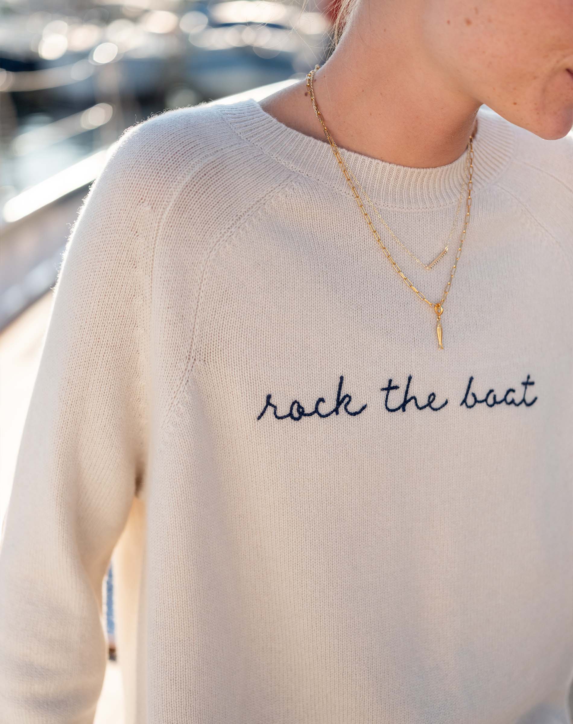 Person wearing a cream sweater with 'rock the boat' text and layered necklaces.
