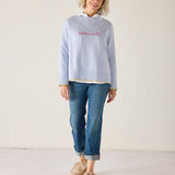 Woman wearing a light blue sweater with 'Optimist' text and blue jeans on a white background