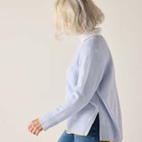 Woman wearing a light blue sweater with a white shirt underneath on a plain background