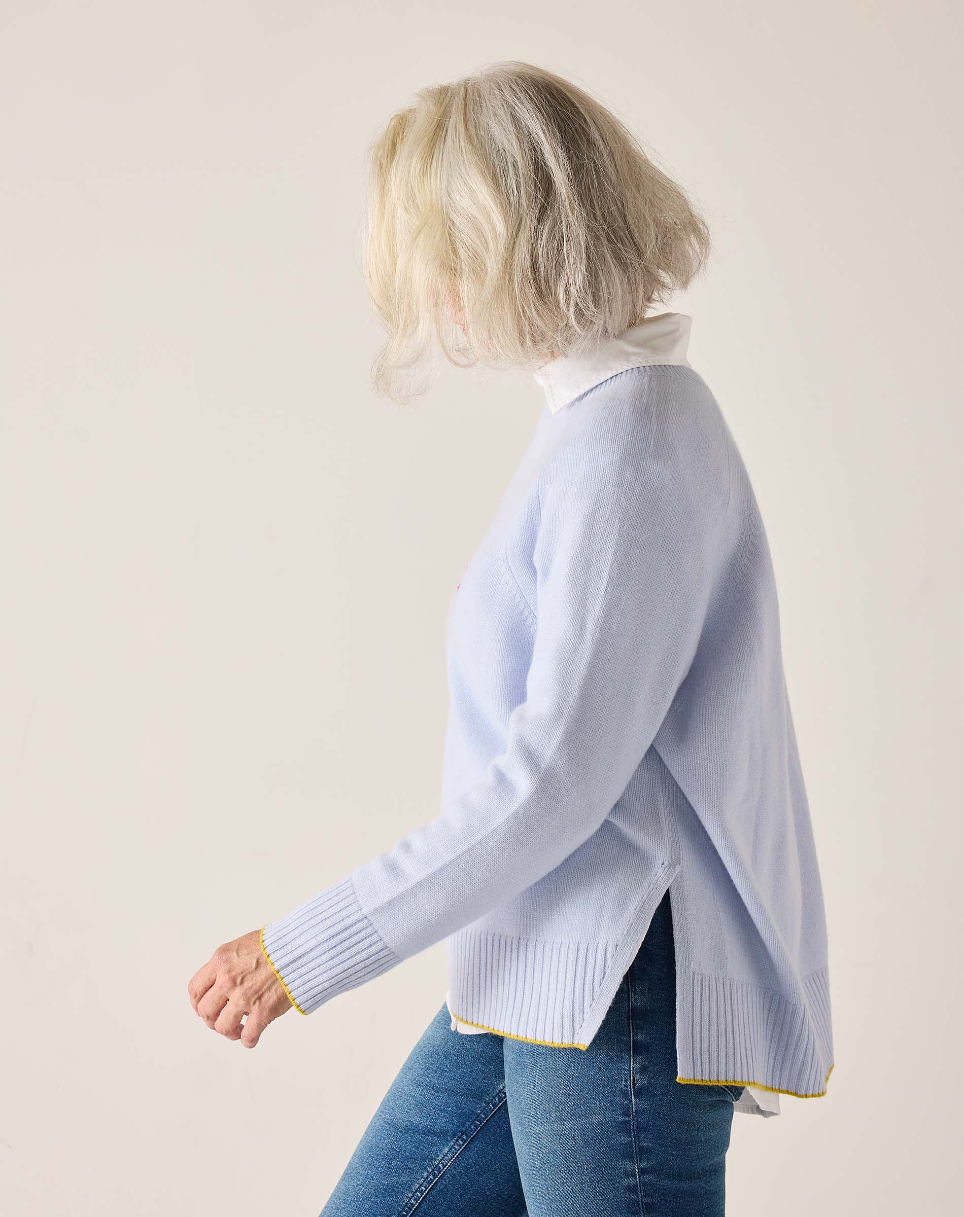 Woman wearing a light blue sweater with a white shirt underneath on a plain background