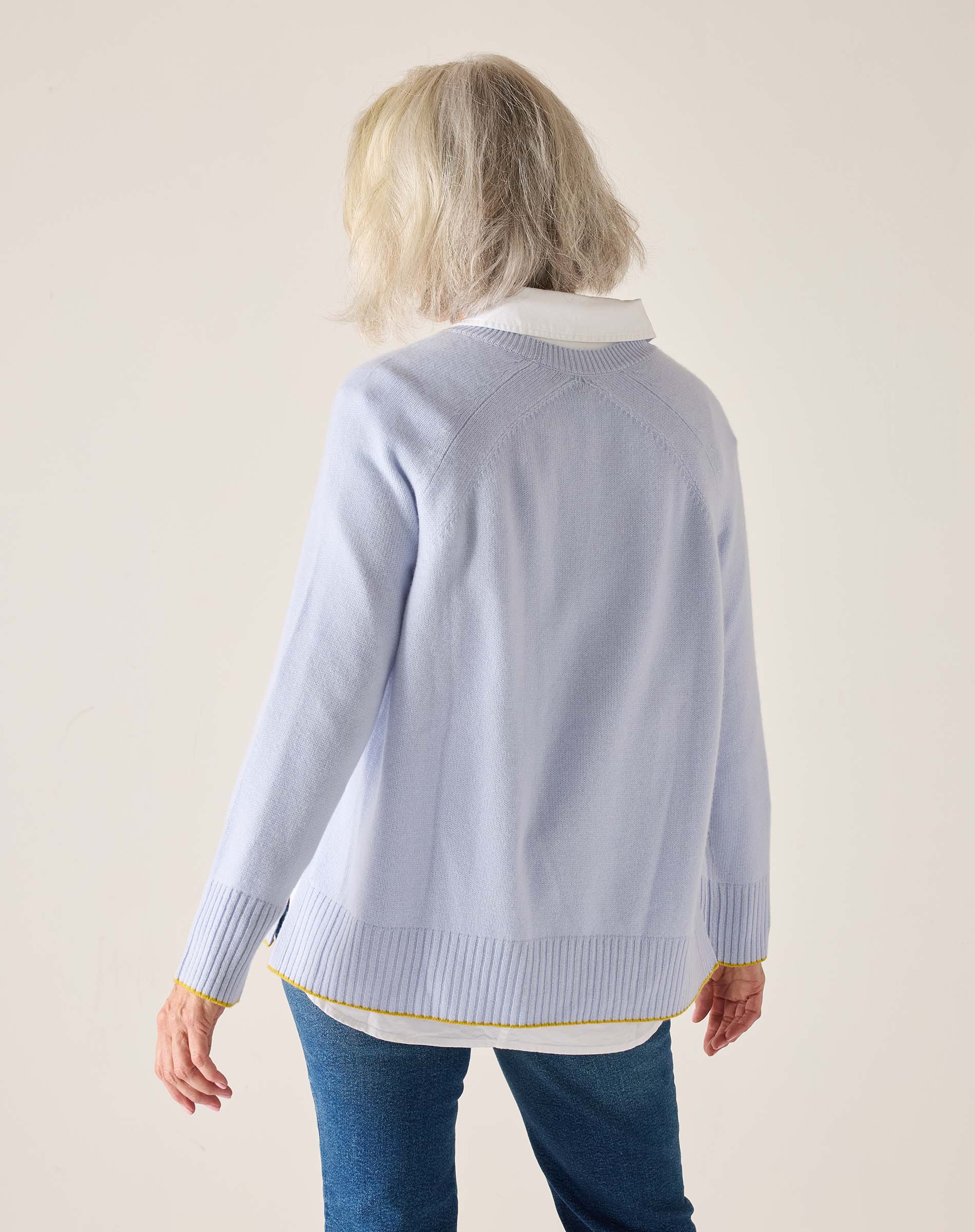 Person wearing a light blue sweater with a white collar on a beige background