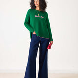Green sweater with pink text 'Weekender' worn by a person on a white background