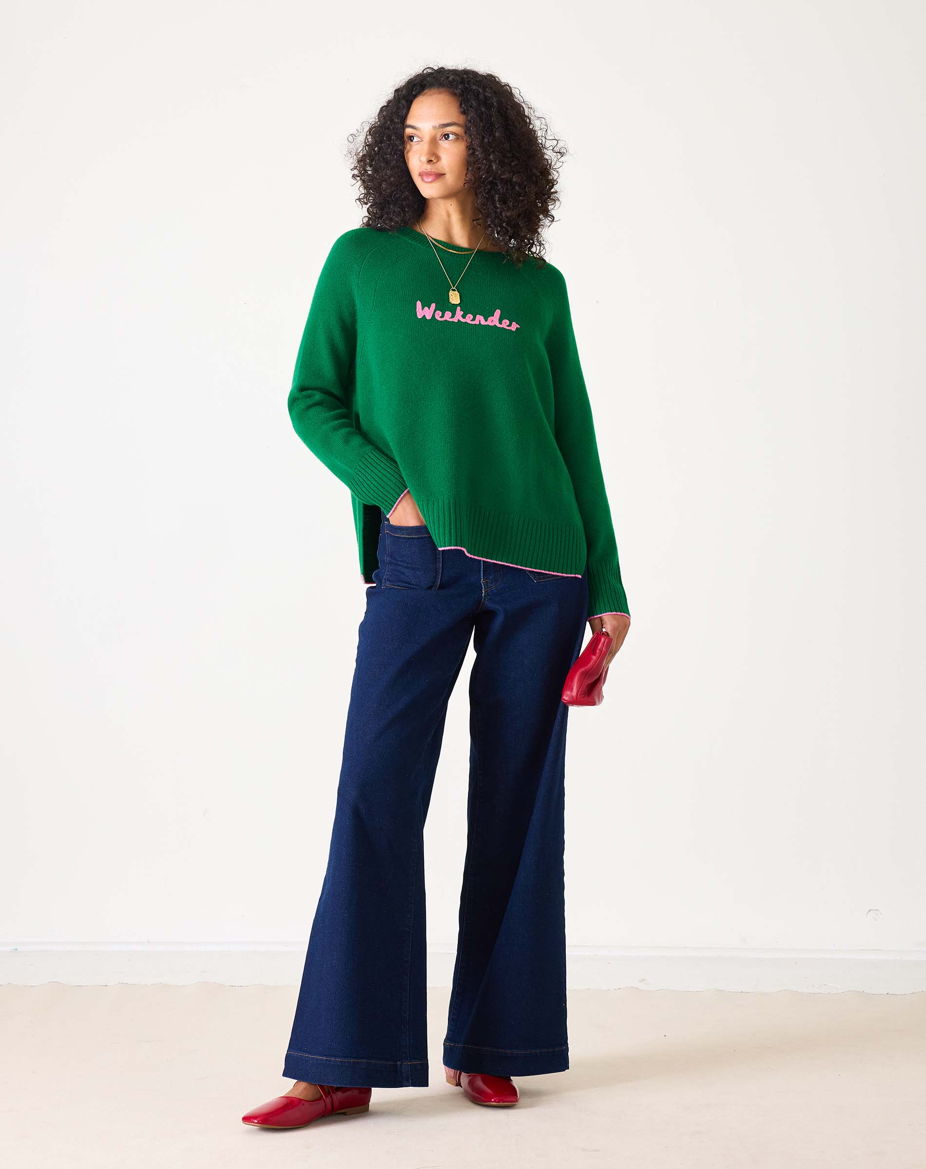 Green sweater with pink text 'Weekender' worn by a person on a white background