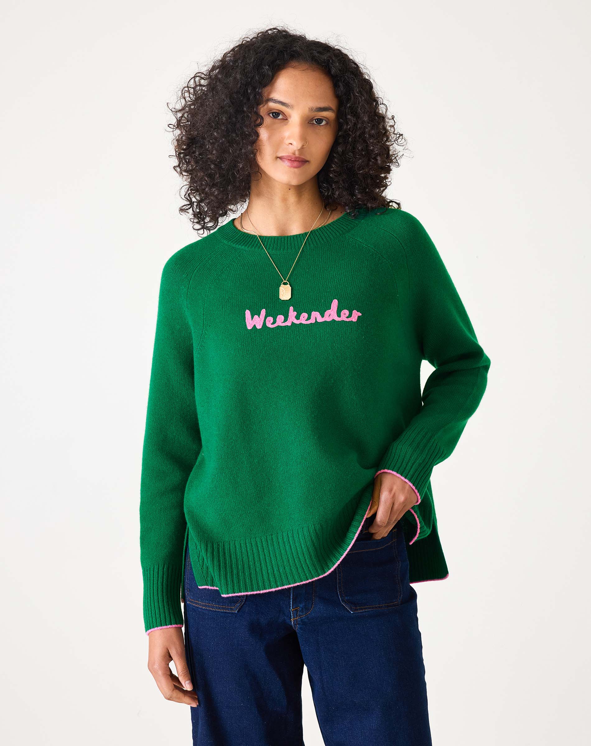 Green sweater with pink text 'Weekender' worn by a person on a white background