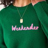 Green sweater with pink text 'Weekender' worn by a person on a white background
