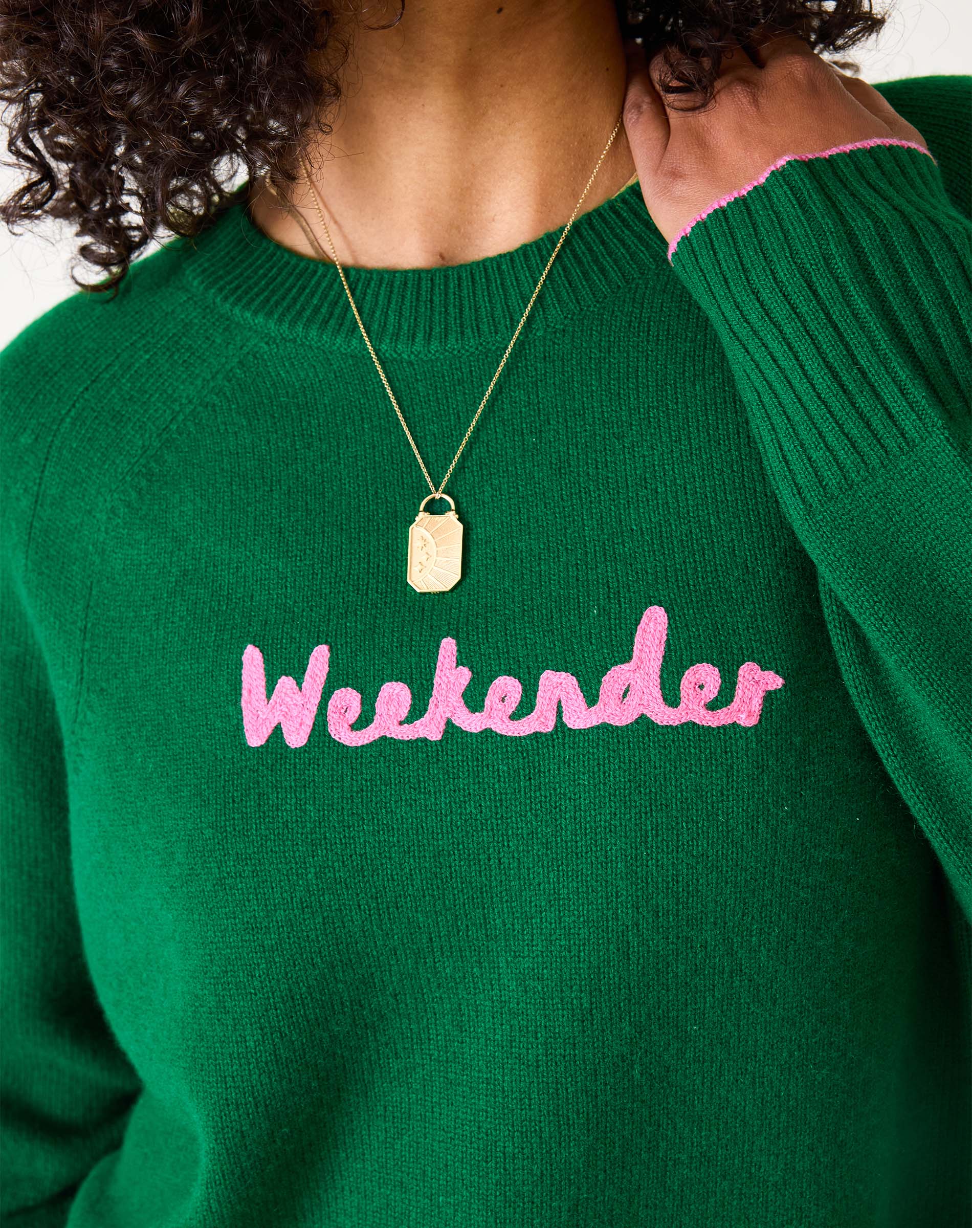 Green sweater with pink text 'Weekender' worn by a person on a white background