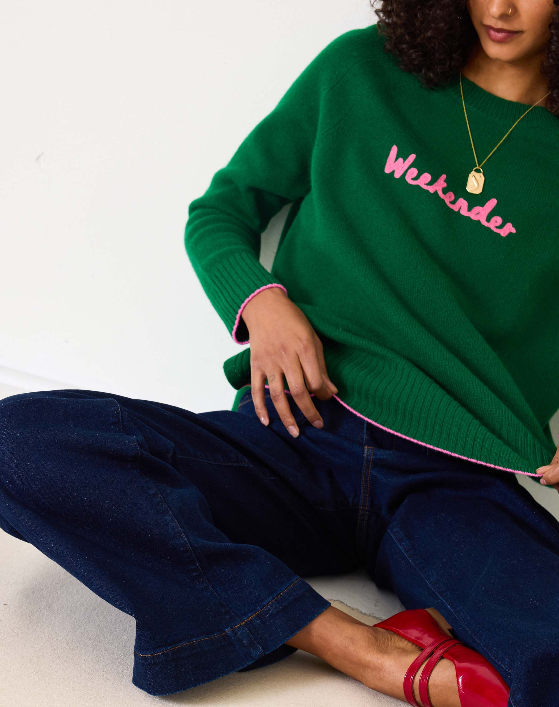 Green sweater with pink text 'Weekender' worn by a person on a white background