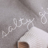 Text 'salty' embroidered on a textured fabric surface