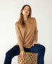 woman wearing mersea banff cashmere sweater in camel sitting on stool