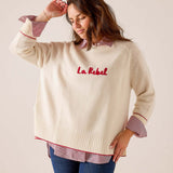Cream oversized knit sweater with red lettering and striped cuffs. Text: La Rebel