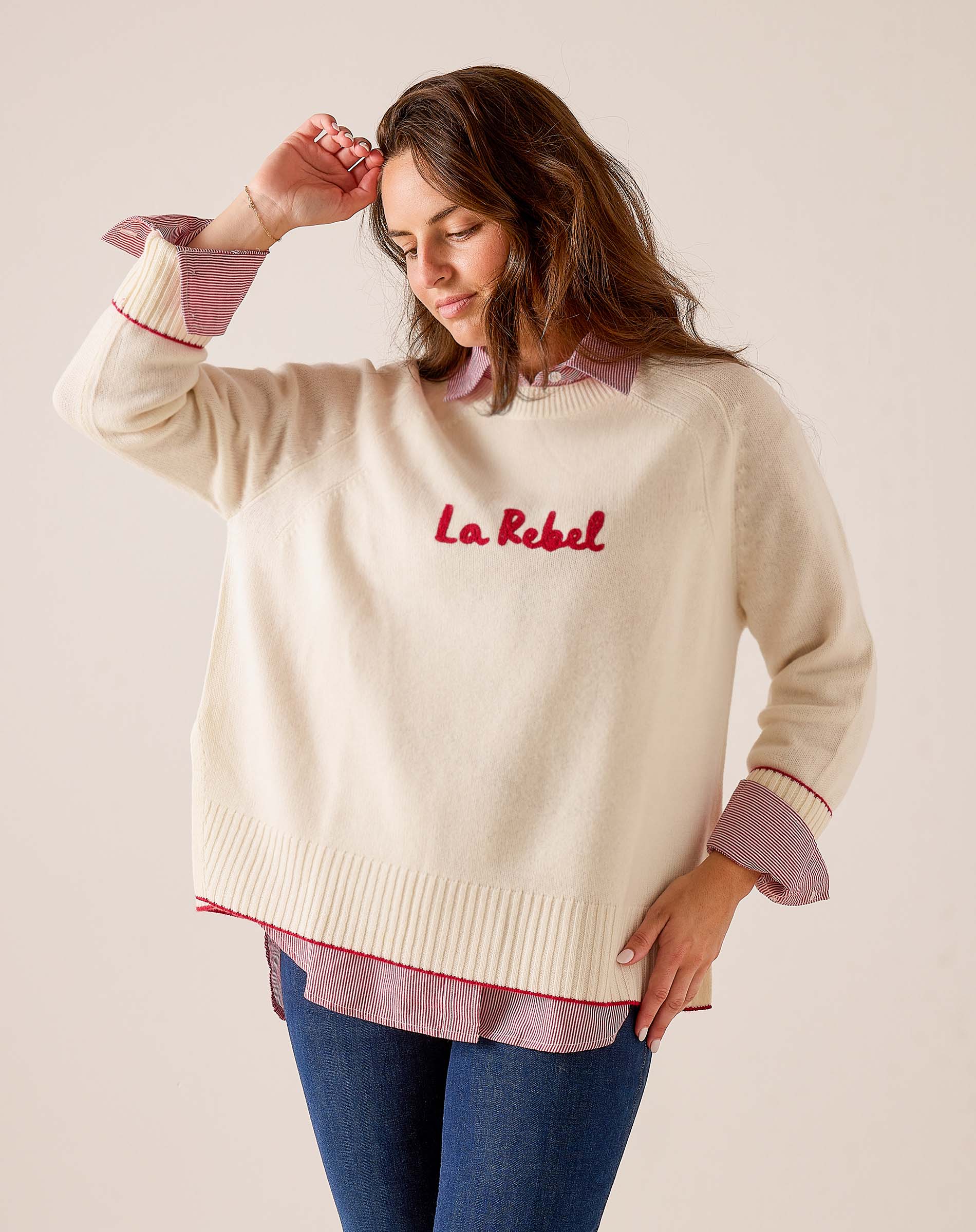 Cream oversized knit sweater with red lettering and striped cuffs. Text: La Rebel