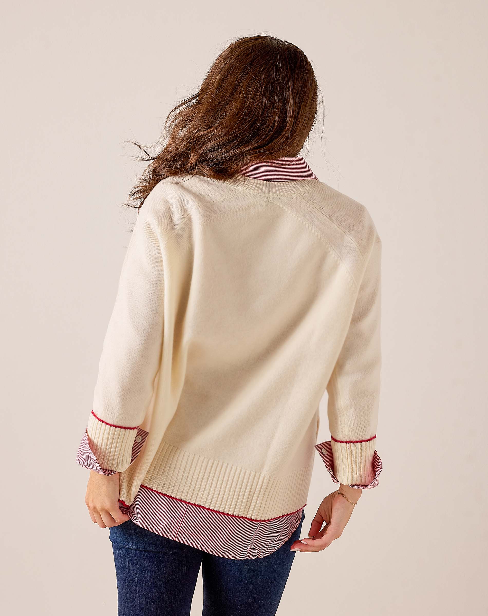 Back view of a ivory knit sweater featuring a striped contrast hem and cuffs with red trim.