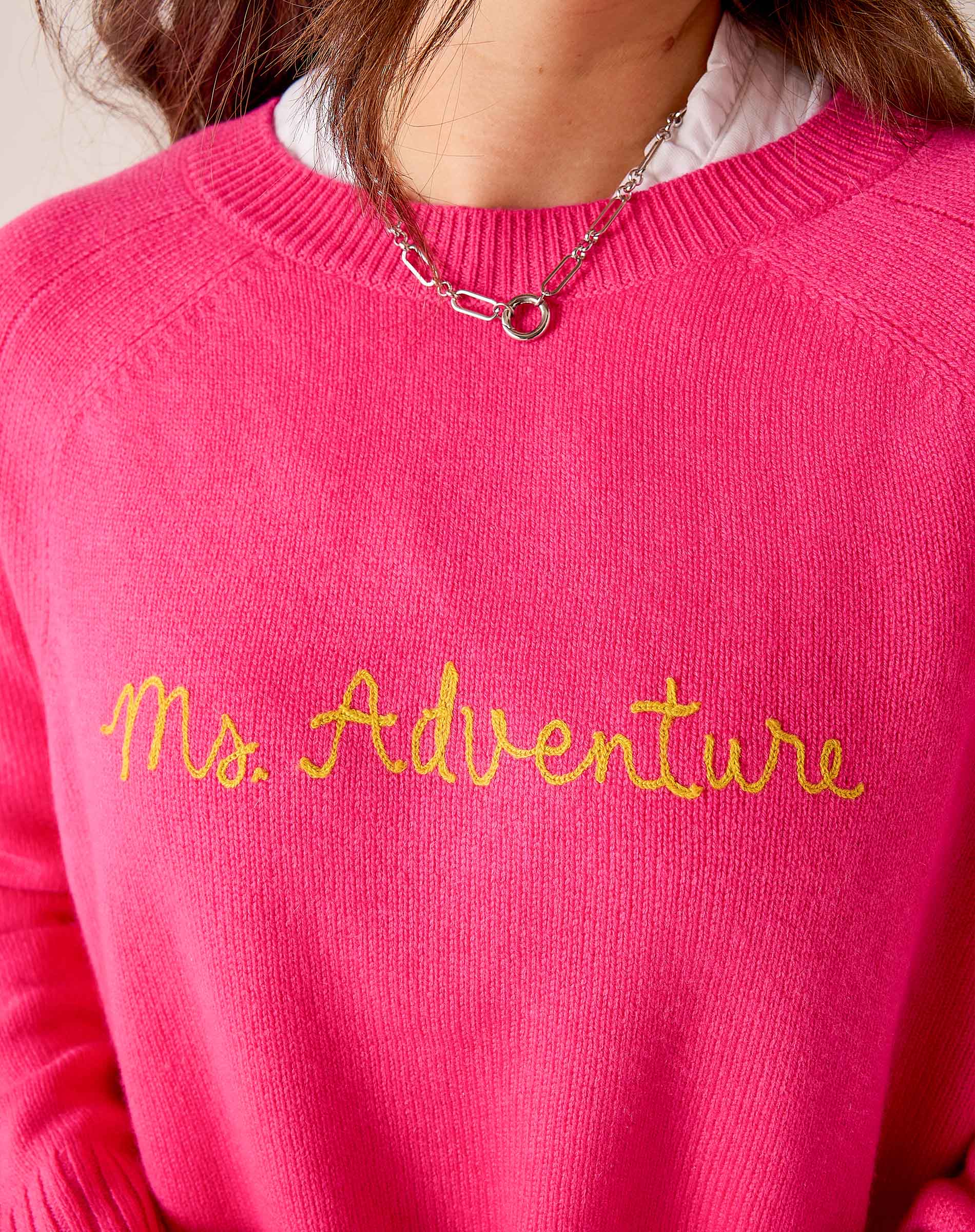 Hot pink knit sweater with a crew neck and 'Ms. Adventure' embroidered in yellow script. Text: Ms. Adventure