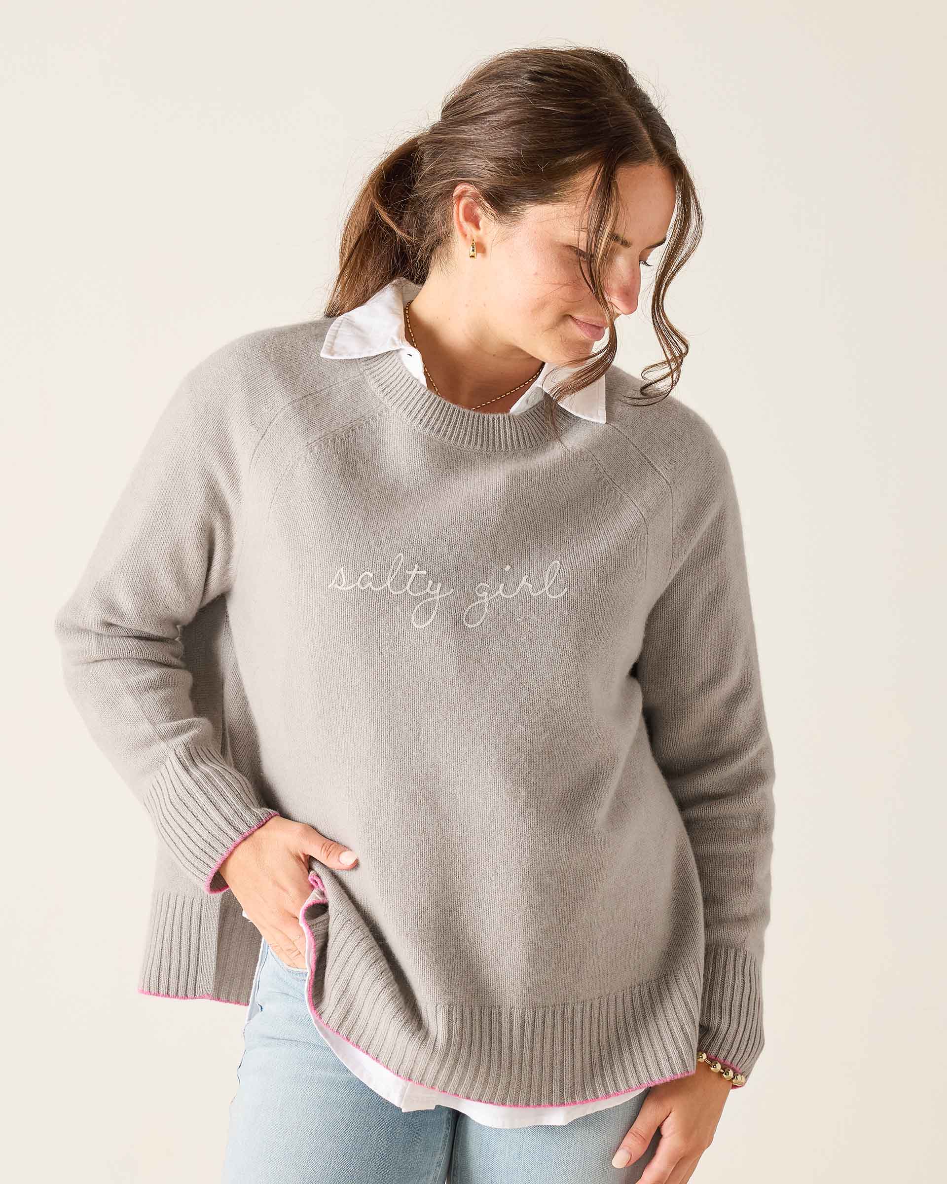 Woman wearing a gray sweater with 'salty girl' text on a plain background