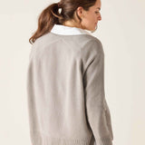 Woman wearing a light gray sweater with a white collar against a plain background