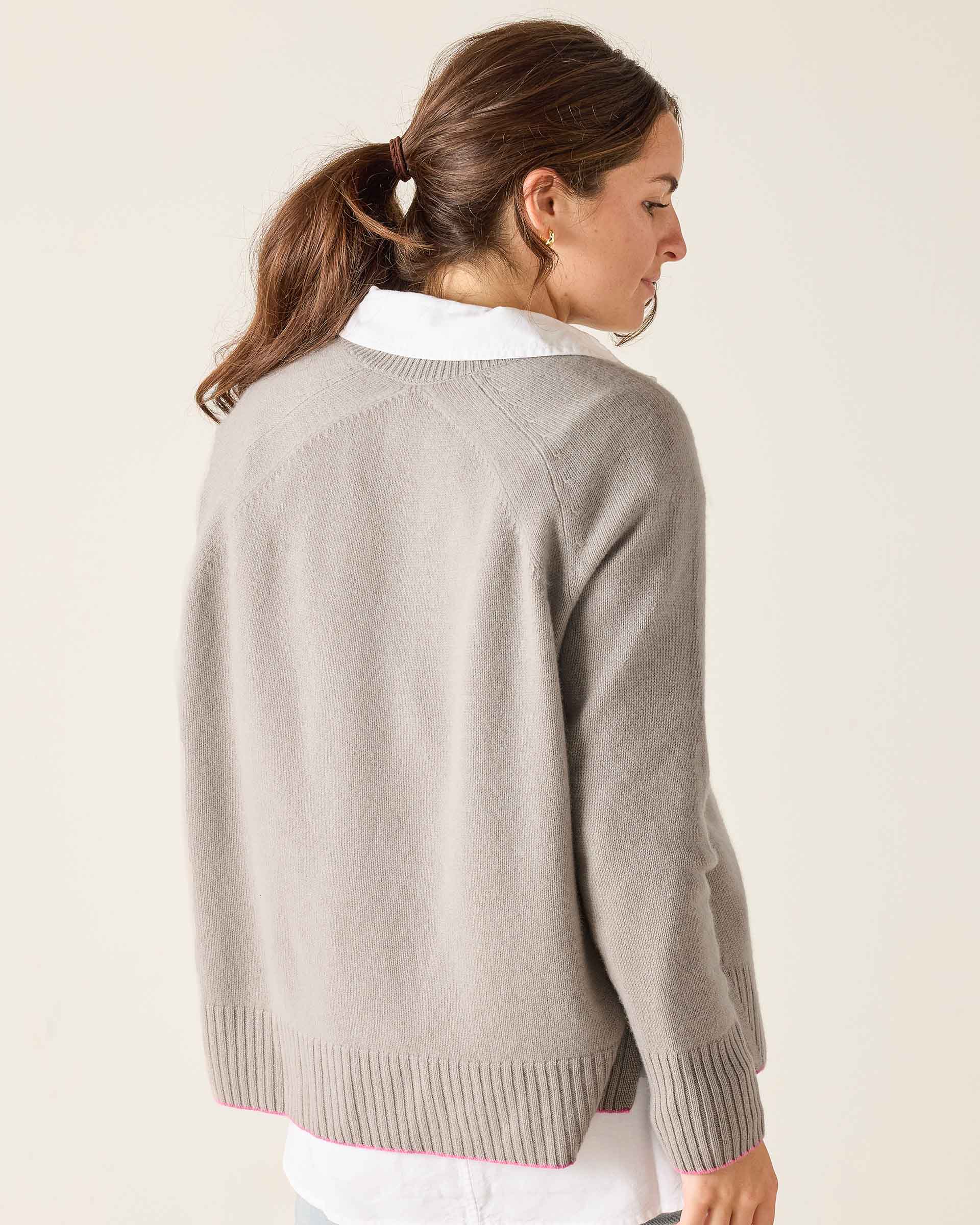 Woman wearing a light gray sweater with a white collar against a plain background