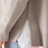 Close-up of a person wearing a beige sweater with pink trim, white shirt, and blue jeans.