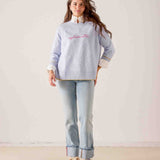 Women's travel-friendly sky blue knit sweater with 'optimistic' embroidery and striped trim. Text: optimistic