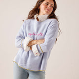 Sky blue oversized knit sweater with 'optimiste' script and yellow-trimmed ribbed details. Text: optimiste.