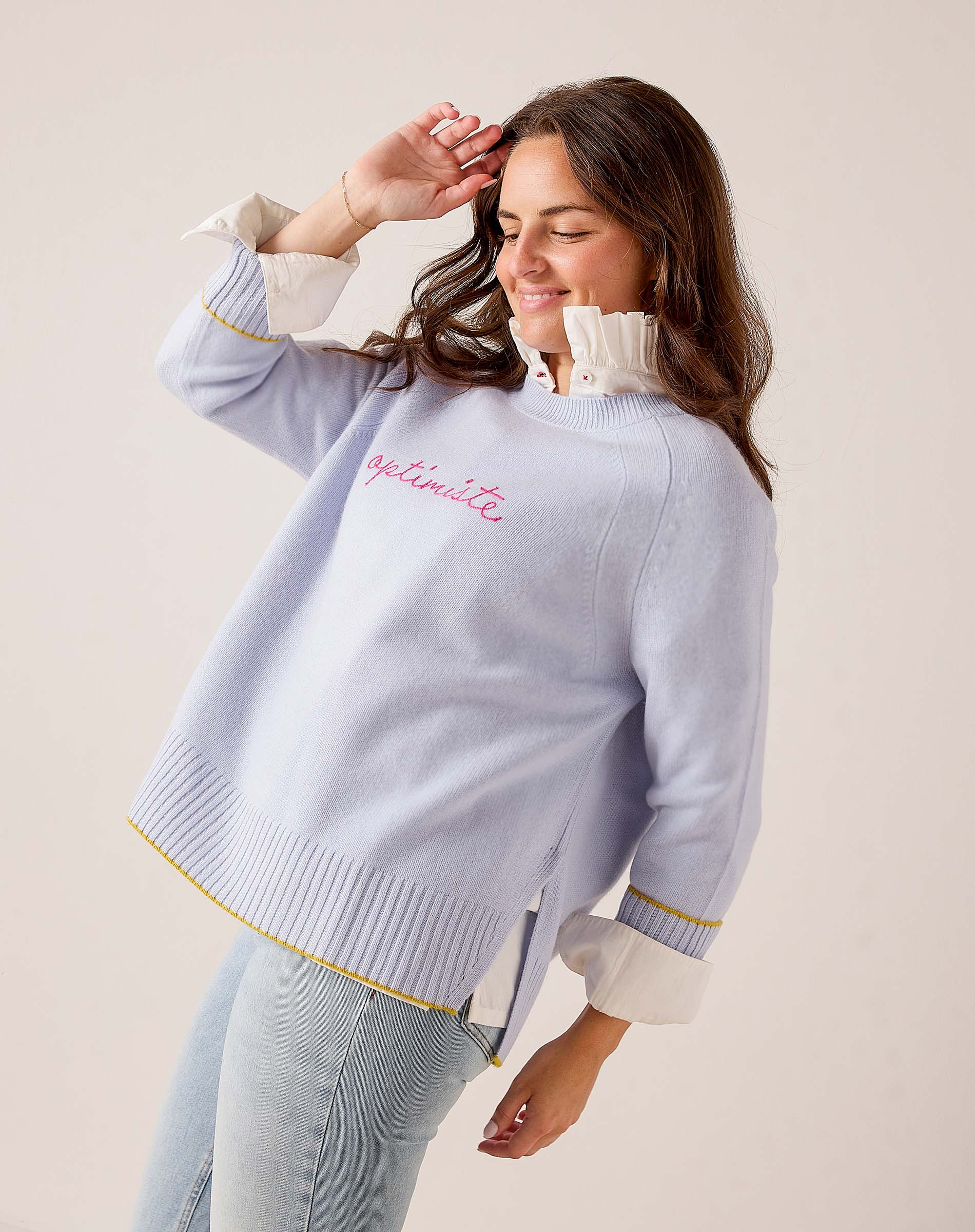 Sky blue knit sweater with ruffled neckline and 'optimiste' text on chest. Text: optimiste