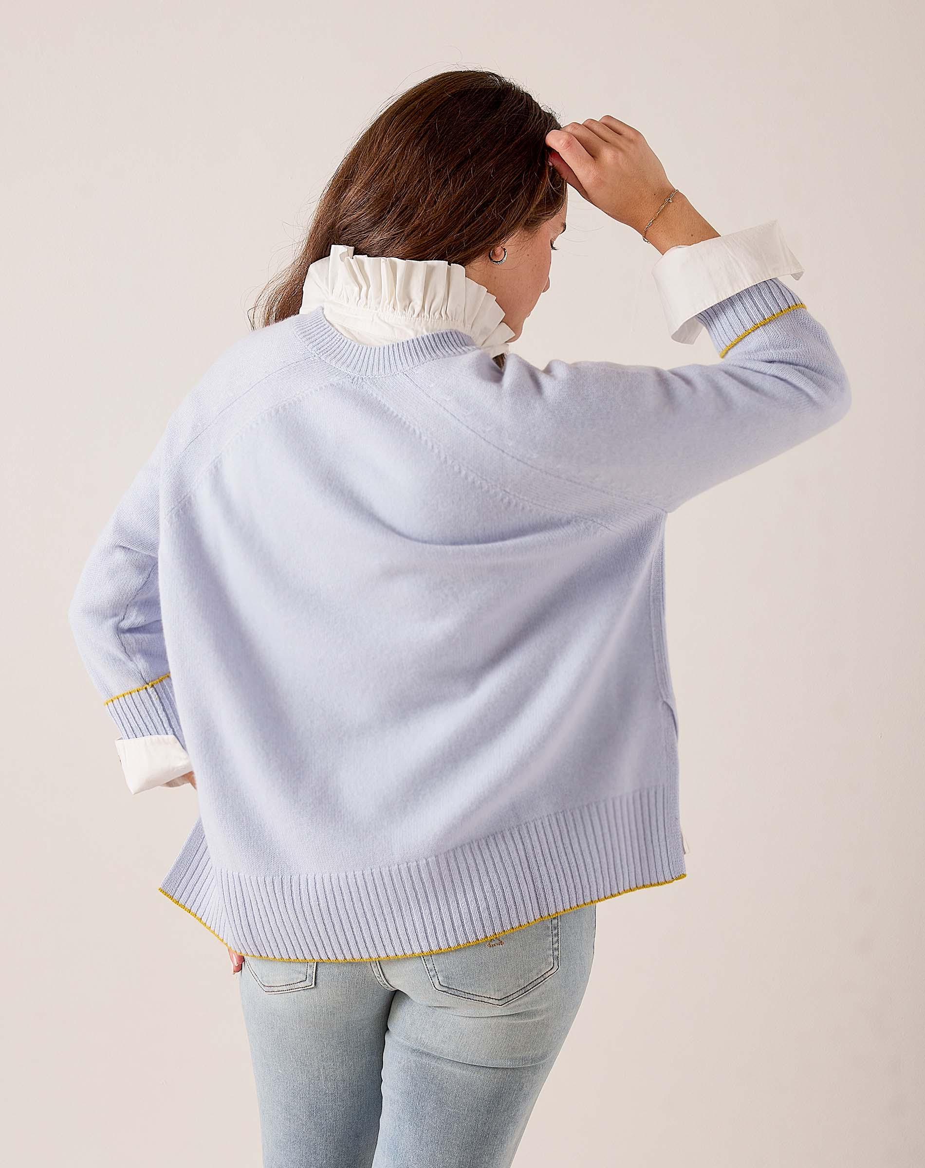 Sky blue knit sweater with a tiered hem, yellow striped trim, and white ruffled collar