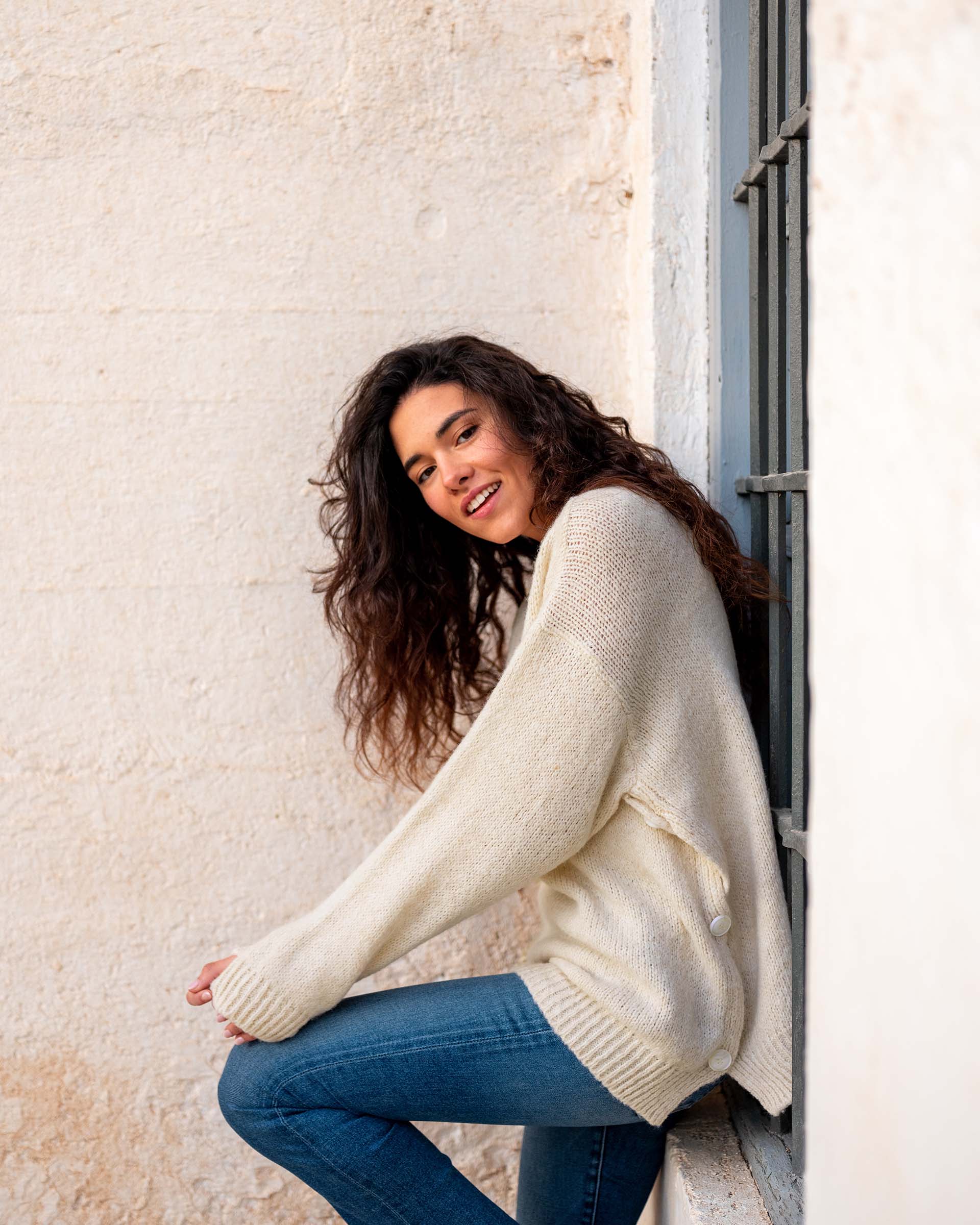woman wearing mersea bari side button buttercream sweater standing against window