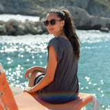 Woman sitting on a beach chair by the water wearing sunglasses.