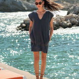 Woman in a dark blue dress standing by a body of water with rocks in the background