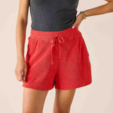 Person wearing red shorts and a black top on a beige background