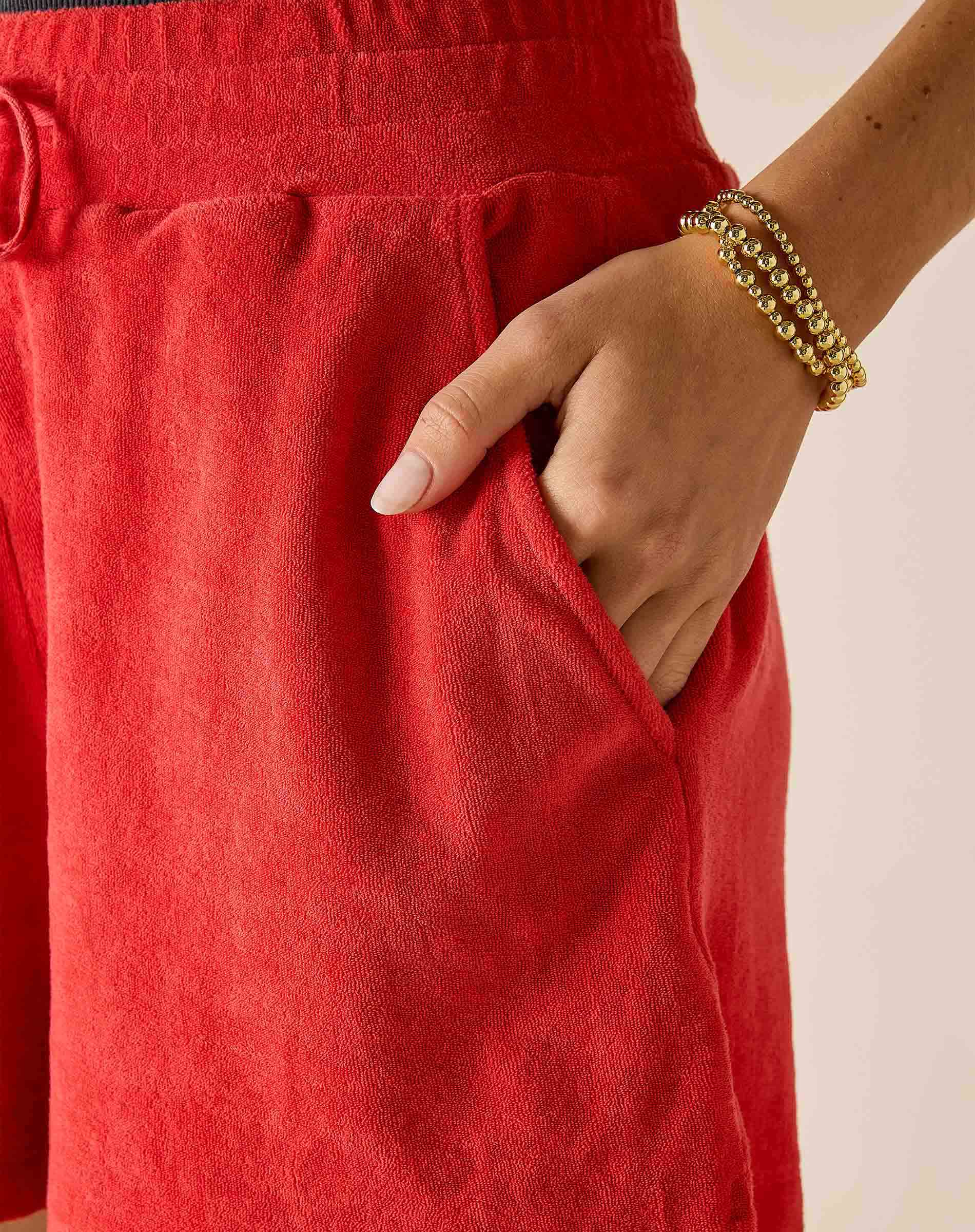 Person wearing red pants with a gold bracelet on a neutral background