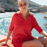 Woman in a red outfit sitting by a body of water with mountains in the background