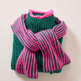 Women's travel-friendly forest green knit sweater with a pink and green striped ribbed scarf draped over the shoulders.