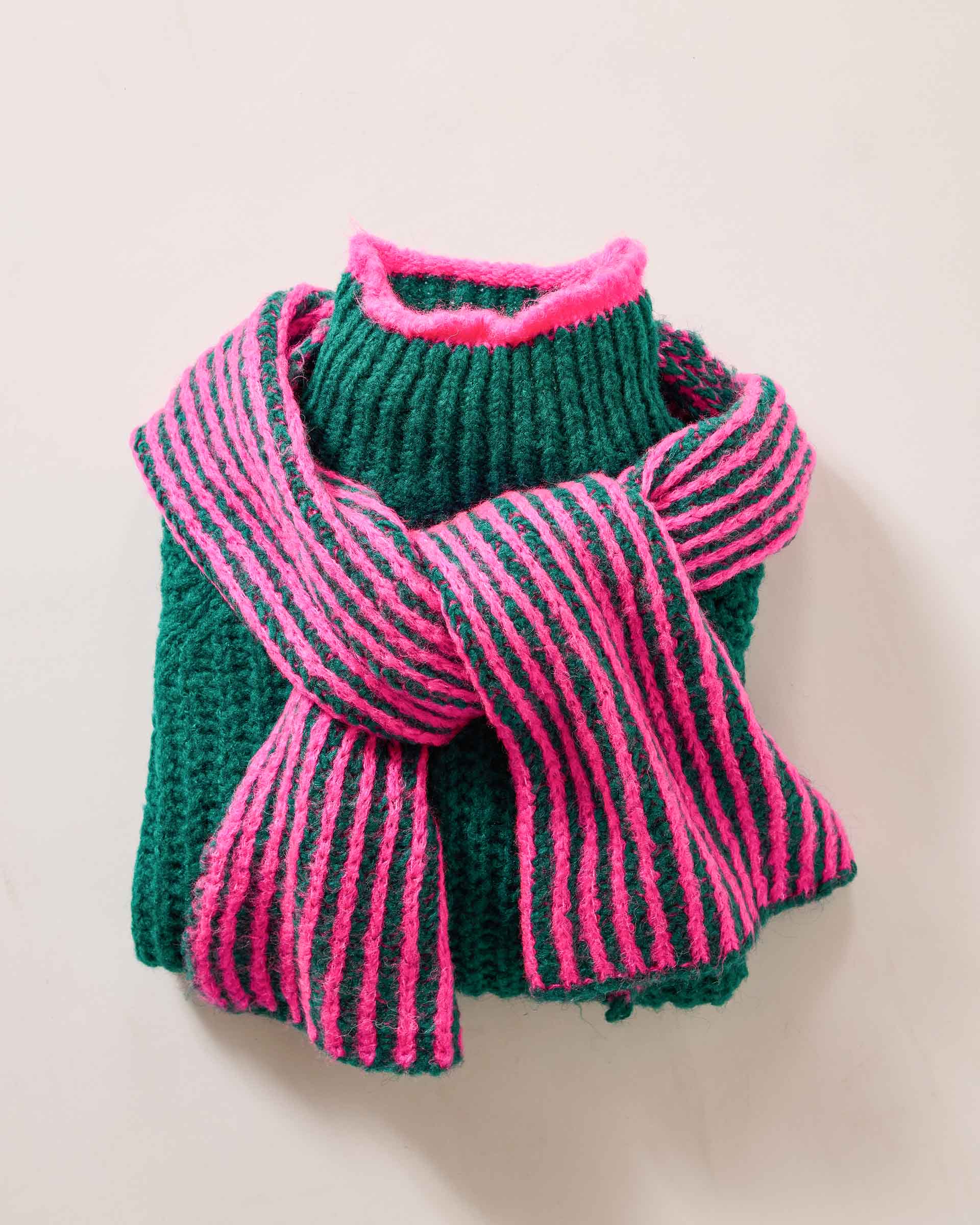 Women's travel-friendly forest green knit sweater with a pink and green striped ribbed scarf draped over the shoulders.