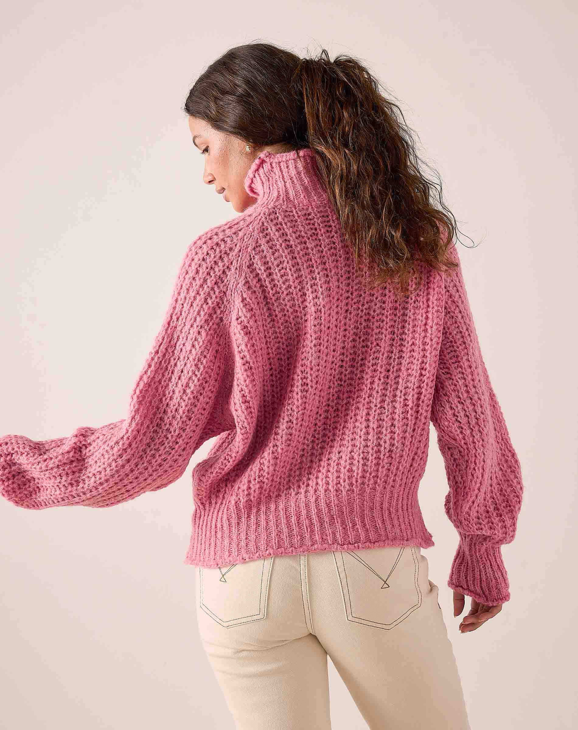 Soft pink chunky knit sweater with a high neck and wide sleeves.