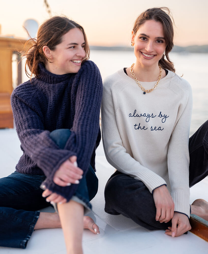 Two women sitting together with one wearing a sweater that says 'always by the sea'.