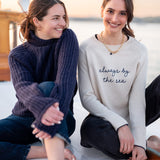 Two women sitting together with one wearing a sweater that says 'always by the sea'.