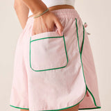 Pink apron with green trim worn by a person on a neutral background